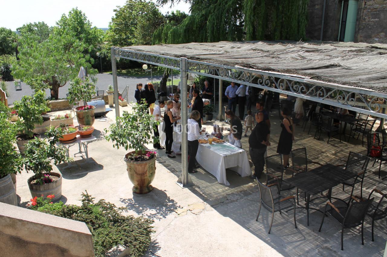Des personnes rassemblées sous une pergola dans une cour extérieure, avec des tables et des plantes en pot.