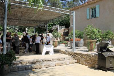 Groupe de personnes rassemblées dans une cour extérieure verdoyante devant un bâtiment en pierre avec des volets bleus.