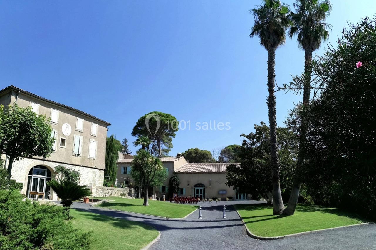 Bâtiments en pierre entourés de pelouses, arbres et palmiers sous un ciel bleu clair.