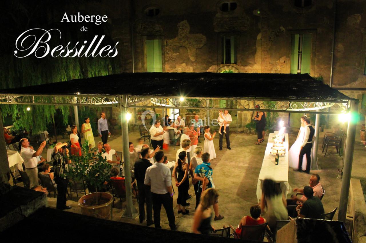 Groupe de personnes rassemblées en soirée sous une pergola éclairée, devant un bâtiment ancien.