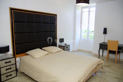 Groupe de personnes rassemblées dans une cour extérieure verdoyante devant un bâtiment en pierre avec des volets bleus.