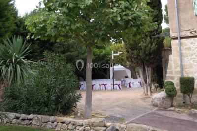 Groupe de personnes rassemblées dans une cour extérieure verdoyante devant un bâtiment en pierre avec des volets bleus.
