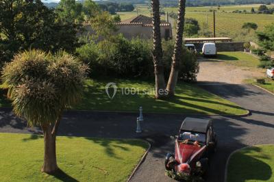 Groupe de personnes rassemblées dans une cour extérieure verdoyante devant un bâtiment en pierre avec des volets bleus.