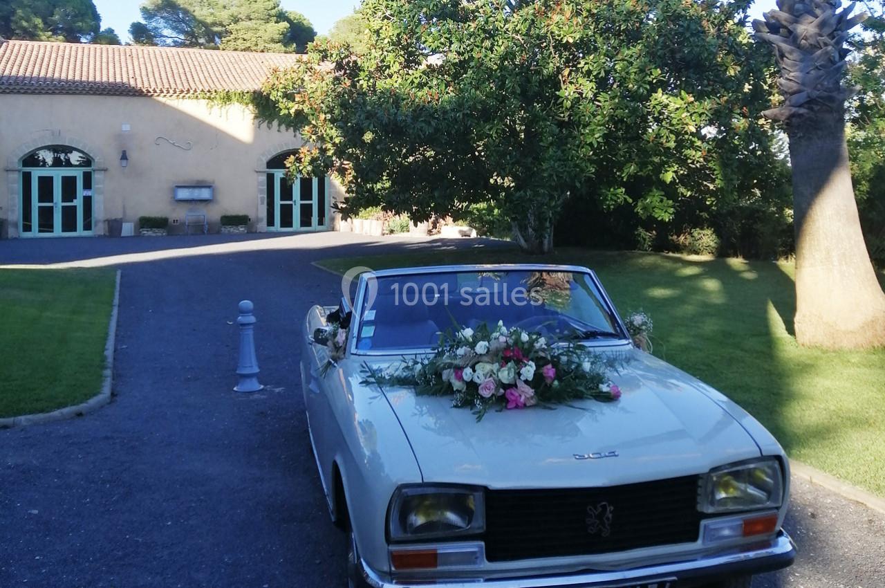 Voiture ancienne blanche décorée de fleurs, stationnée devant un bâtiment avec des arches et un jardin arboré.