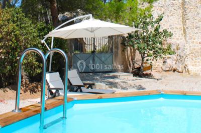 Groupe de personnes rassemblées dans une cour extérieure verdoyante devant un bâtiment en pierre avec des volets bleus.