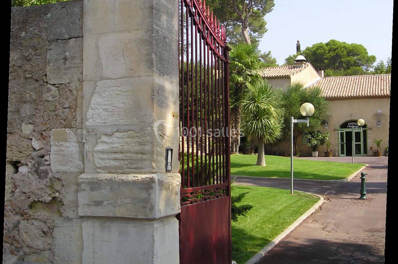 Portail rouge ouvert donnant sur une allée bordée de pelouse et menant à une maison entourée de végétation.
