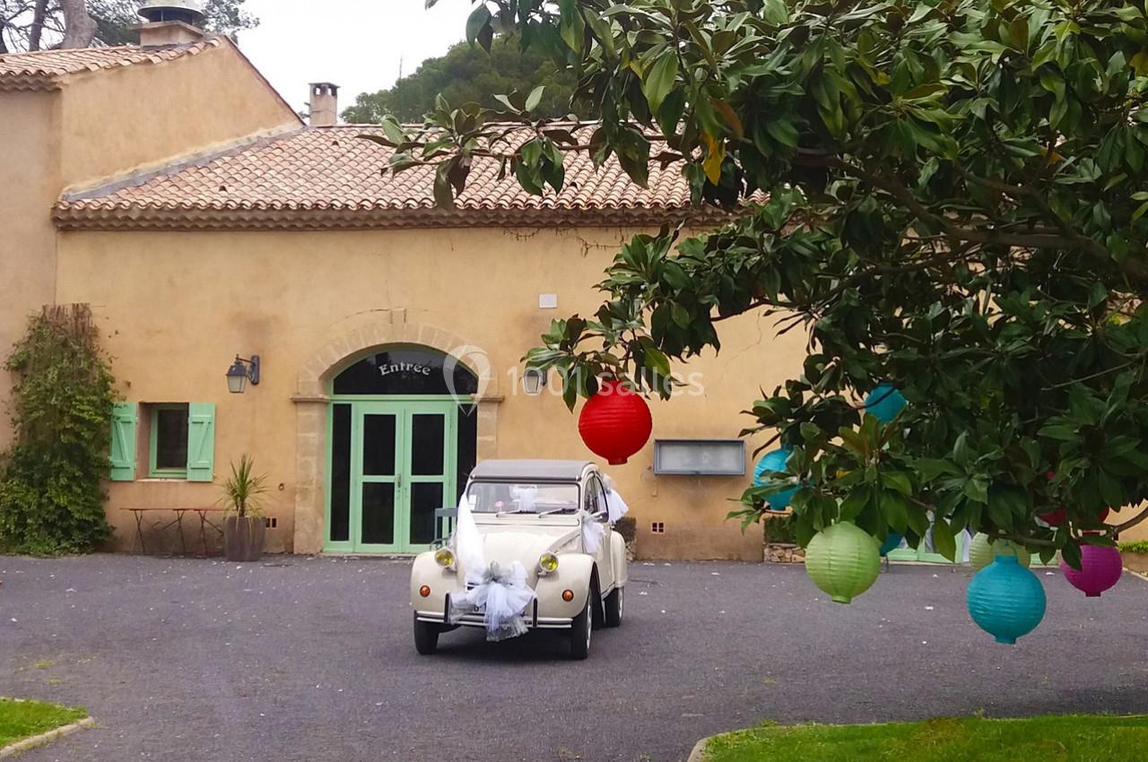 Voiture blanche décorée pour un mariage garée devant un bâtiment en pierre, avec des lanternes colorées suspendues.