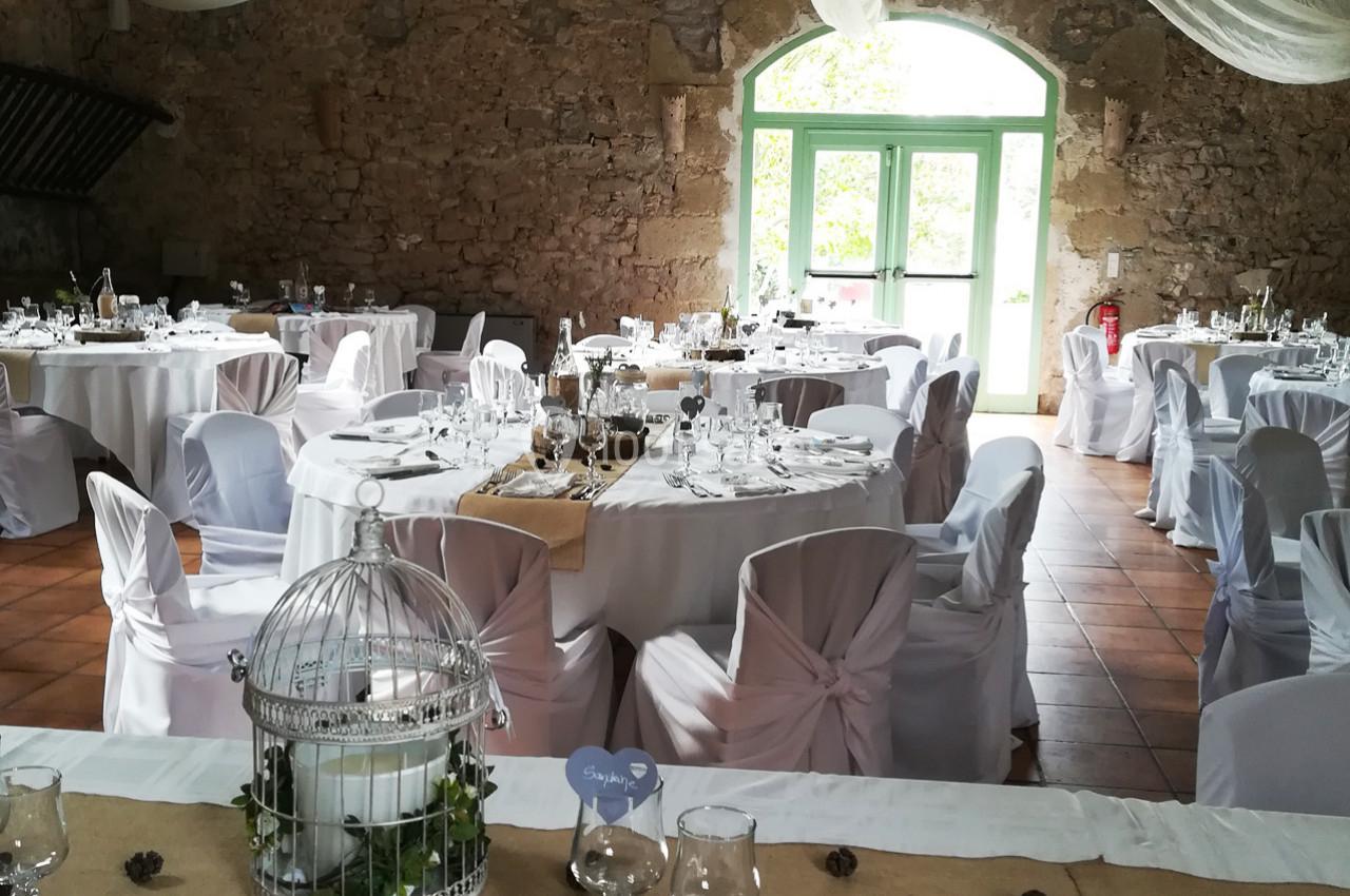 Salle de réception décorée avec des tables rondes dressées, nappes blanches et centre de table avec cage décorative.