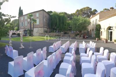 Groupe de personnes rassemblées dans une cour extérieure verdoyante devant un bâtiment en pierre avec des volets bleus.