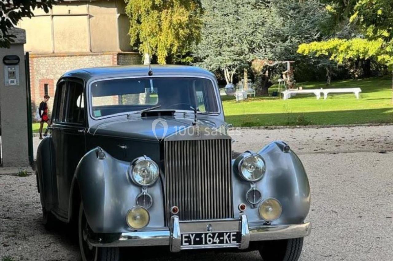 Location salle Villampuy (Eure-et-Loir) - Domaine de la Rainville #34 Voiture ancienne grise stationnée sur un chemin gravillonné, entourée d'arbres et d'un bâtiment en arrière-plan.
