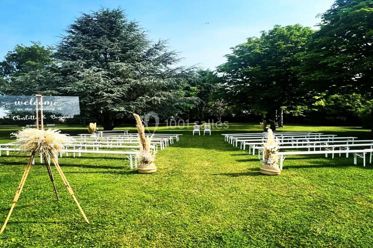 Location salle Villampuy (Eure-et-Loir) - Domaine de la Rainville #4 Chaises blanches alignées en extérieur sur une pelouse, entourées d'arbres, avec un panneau de bienvenue à gauche.