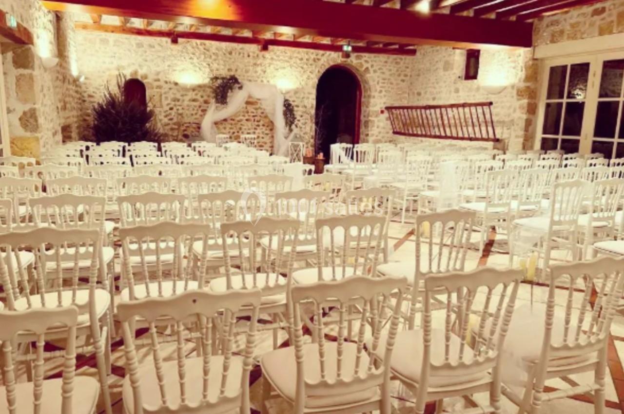 Location salle Villampuy (Eure-et-Loir) - Domaine de la Rainville #41 Salle de réception en pierre avec des chaises blanches alignées et une décoration légère en arrière-plan.