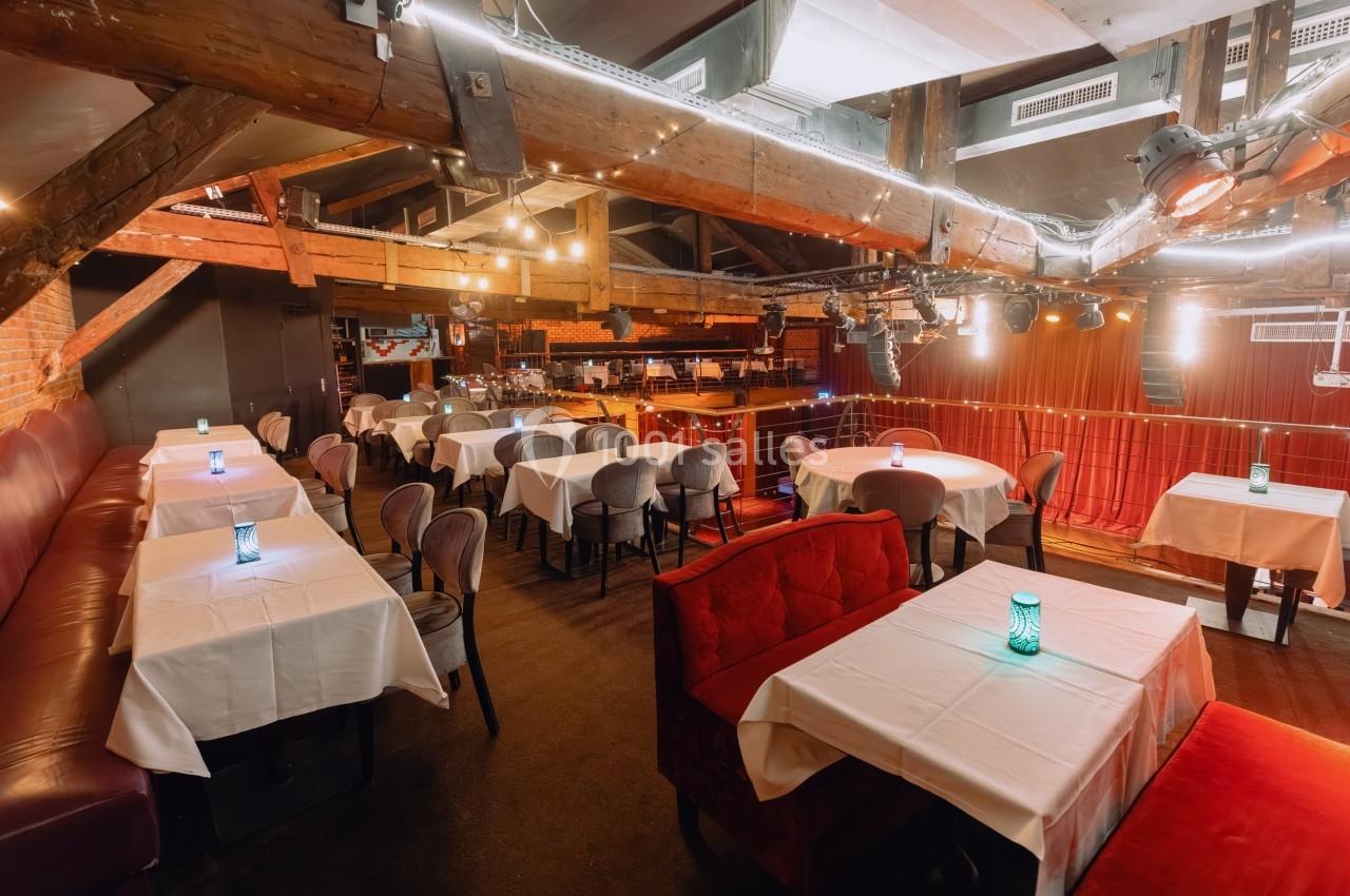 Salle de restaurant avec tables dressées, éclairage chaleureux et poutres apparentes au plafond.
