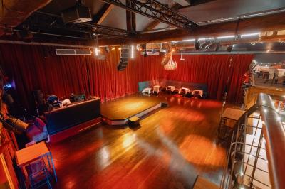 Salle avec un bar central, tabourets alignés, mezzanine avec tables, éclairage chaleureux et poutres apparentes.