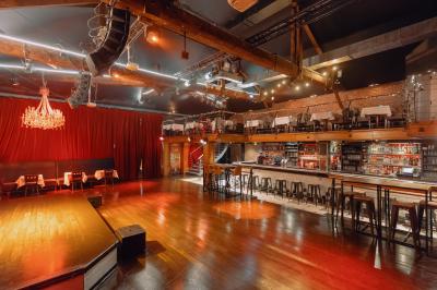 Salle avec un bar central, tabourets alignés, mezzanine avec tables, éclairage chaleureux et poutres apparentes.