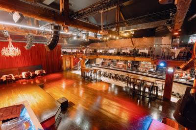 Salle avec un bar central, tabourets alignés, mezzanine avec tables, éclairage chaleureux et poutres apparentes.
