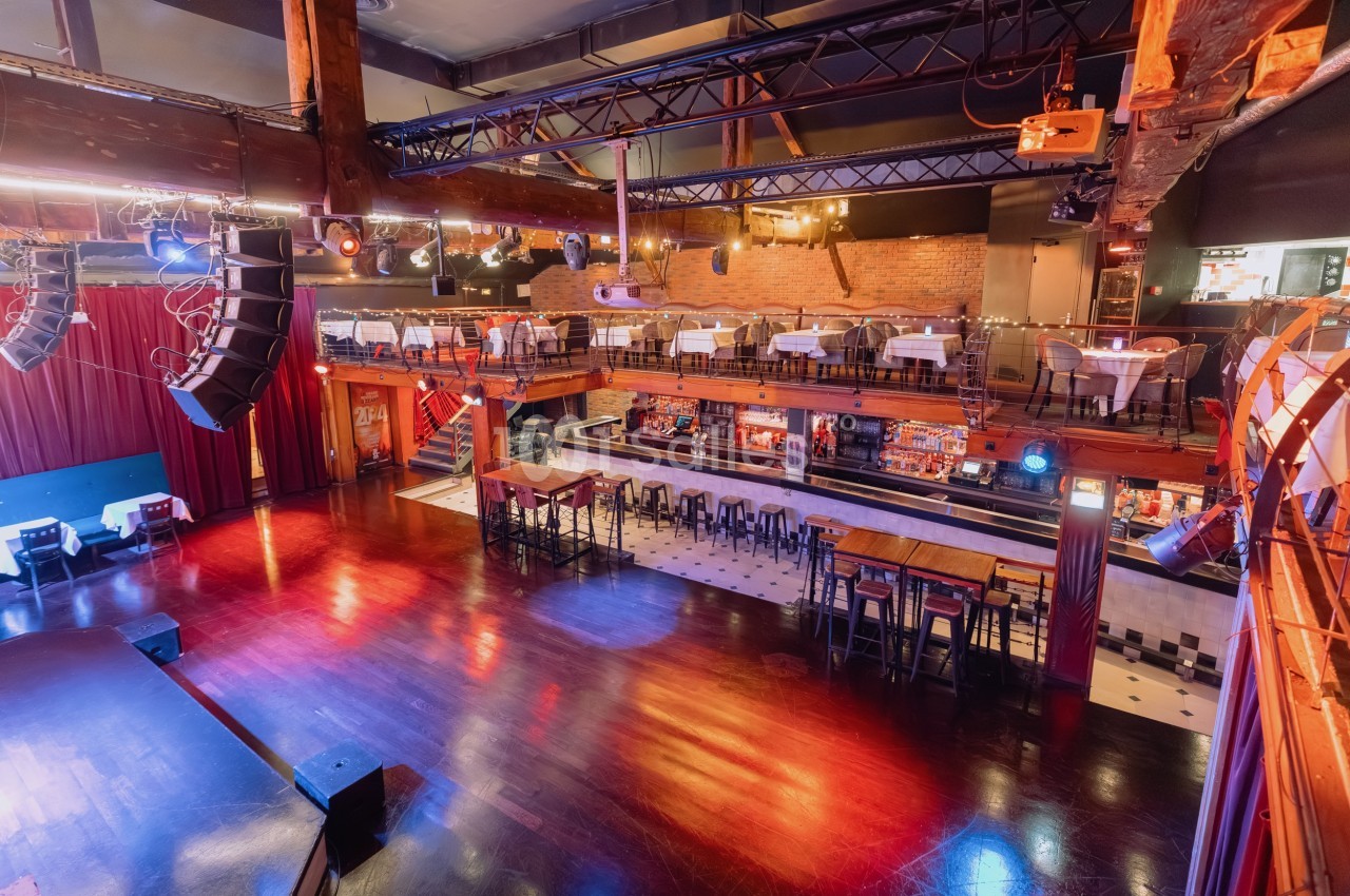 Salle de spectacle avec scène, parquet brillant, tables en mezzanine et éclairage chaleureux.