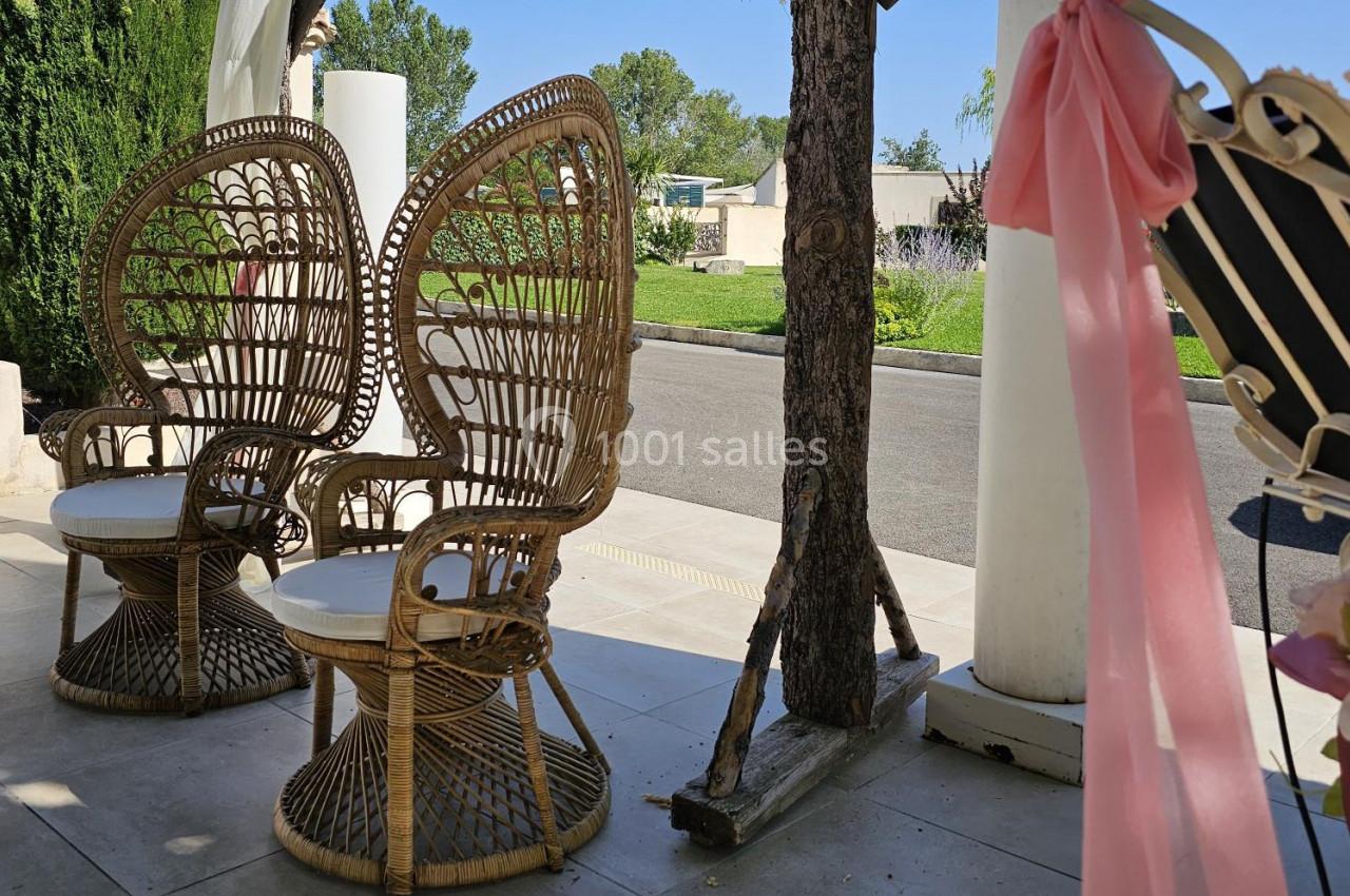 Deux fauteuils en rotin au design ajouré placés sous une pergola, avec un jardin verdoyant en arrière-plan.