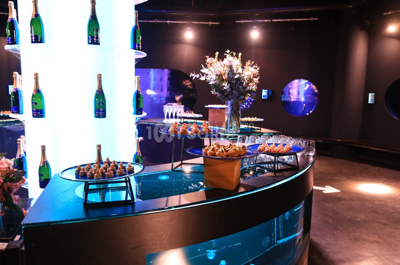 Table garnie de bouchées apéritives, flûtes de champagne et décorations florales dans un espace lumineux et moderne.