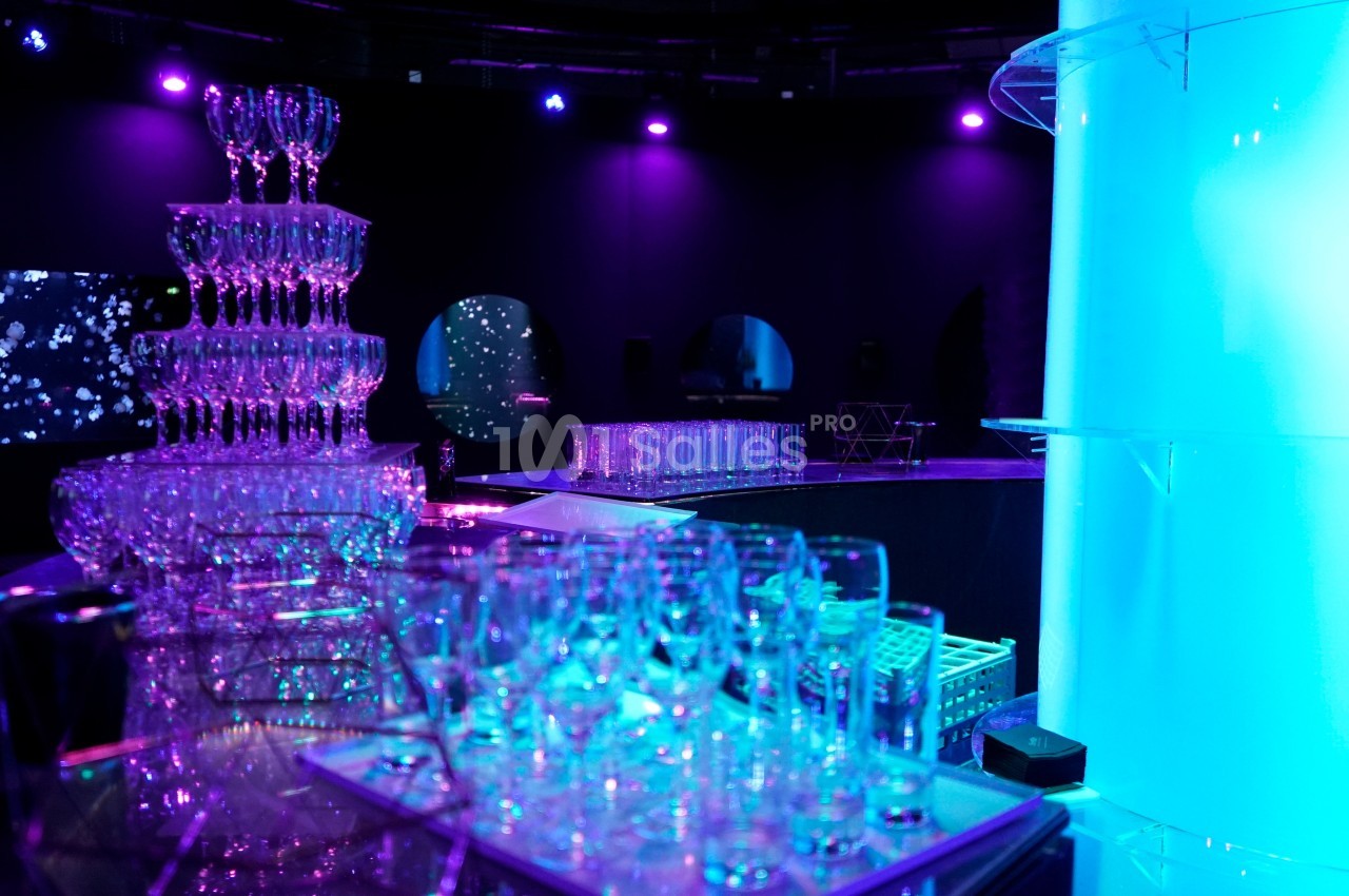 Tour de coupes en verre illuminée dans une ambiance tamisée avec éclairage violet et bleu.