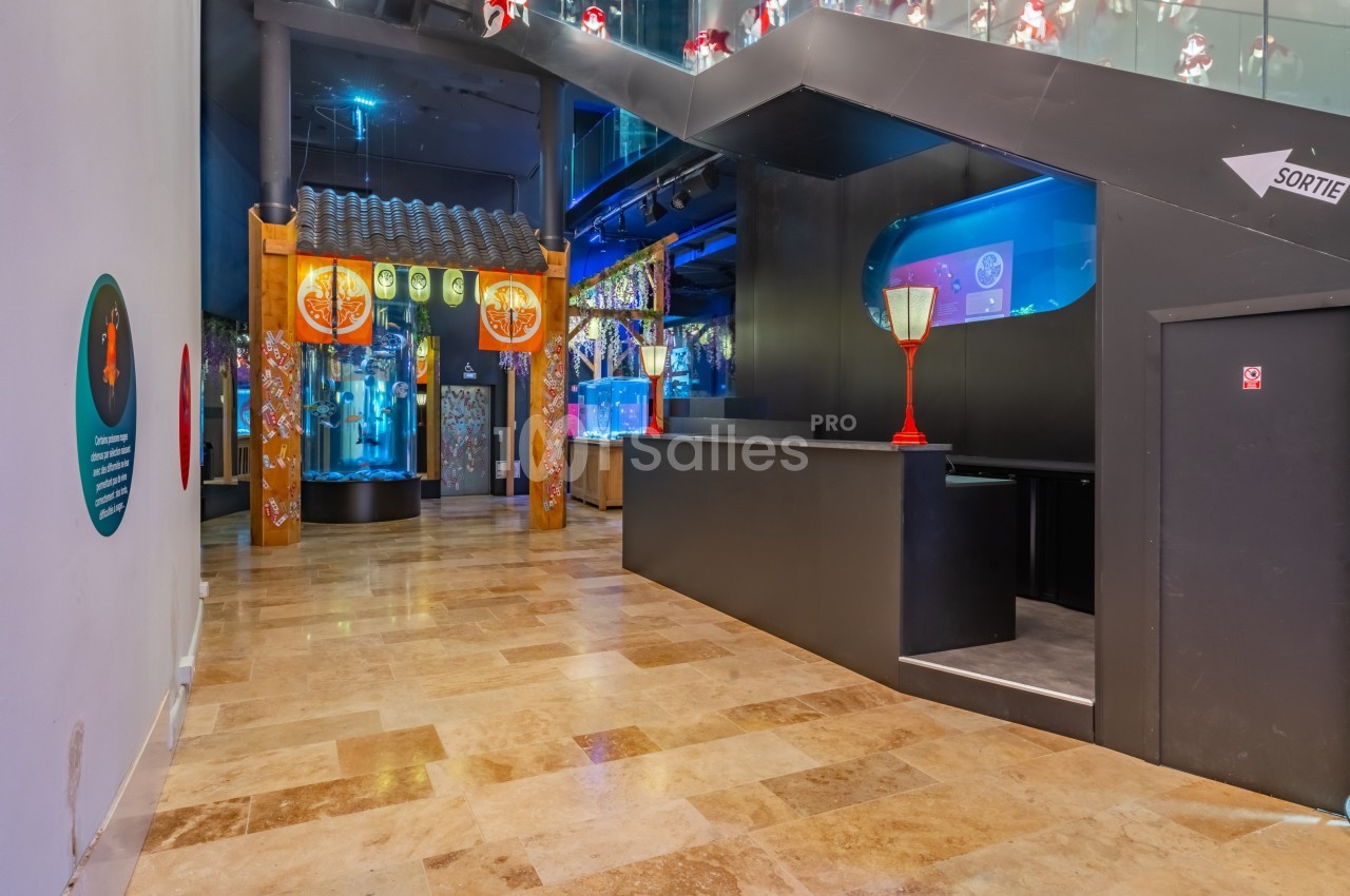 Couloir intérieur avec sol en marbre, décorations asiatiques, aquariums éclairés et panneau indiquant la sortie.