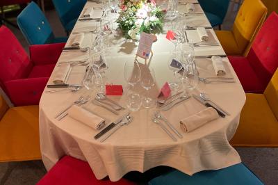 Miniature Location salle Voisins-le-Bretonneux (Yvelines) - La Ferme de Voisins #9 Table dressée avec des verres, couverts et serviettes, entourée de chaises colorées dans une salle lumineuse avec…