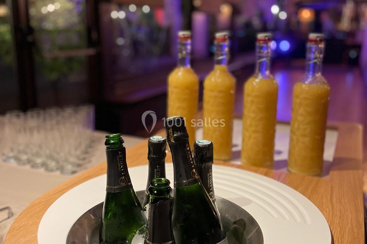Bouteilles de champagne sur glace et carafes de jus disposées sur une table dans un espace éclairé.