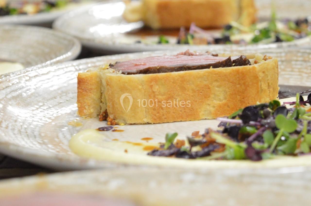 Tranche de bœuf Wellington servie sur une purée, accompagnée de jeunes pousses et d'une garniture croquante.