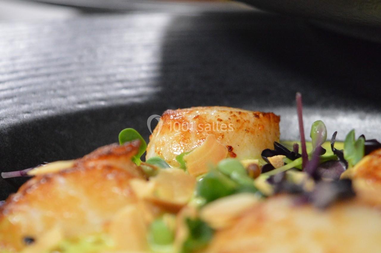 Noix de Saint-Jacques poêlées servies sur une purée verte, garnies de micro-pousses et d'amandes effilées.