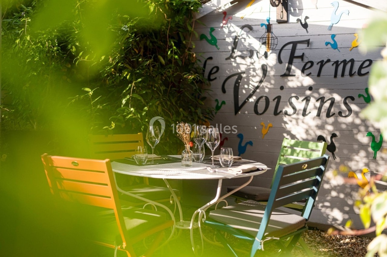 Table de jardin entourée de chaises colorées, disposée dans un coin verdoyant près d'un mur décoré.