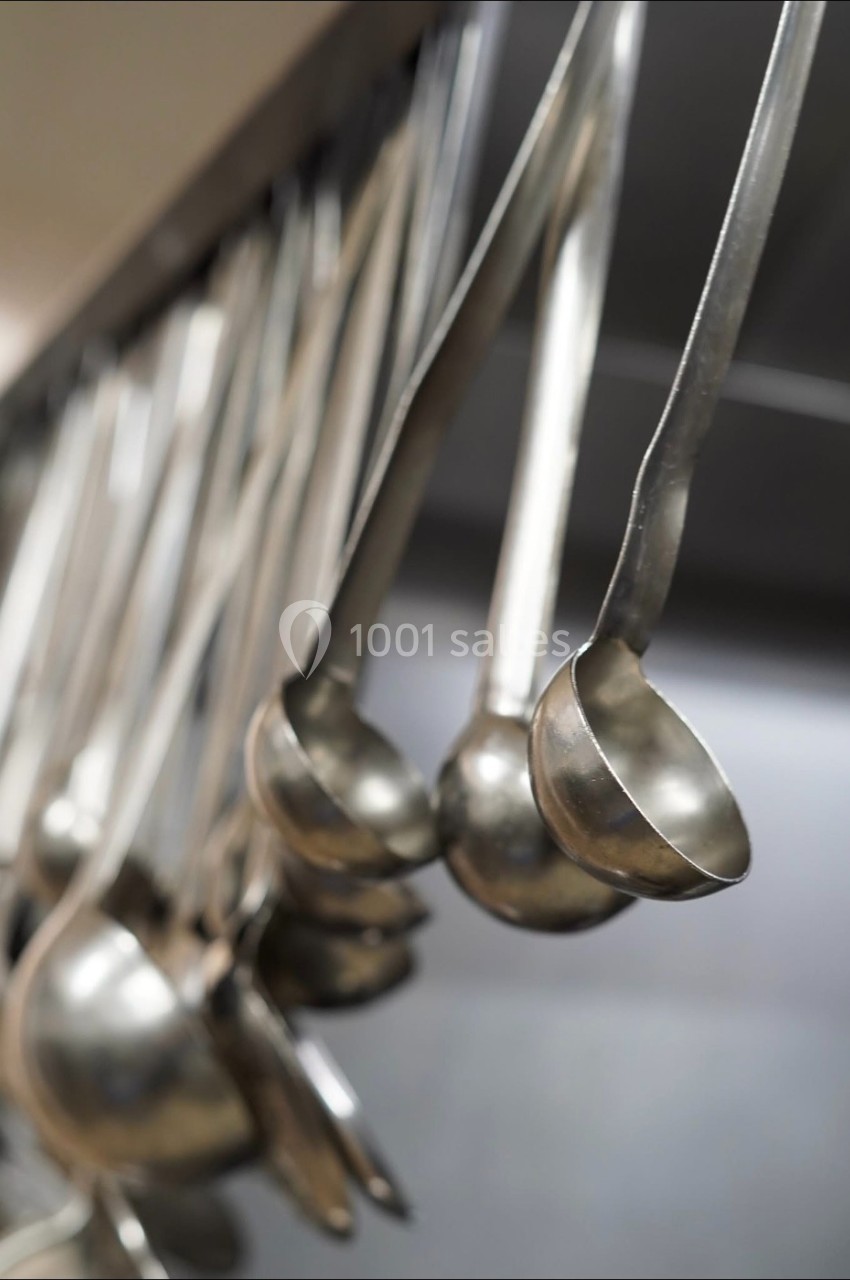 Des louches en métal suspendues à un support dans une cuisine professionnelle.