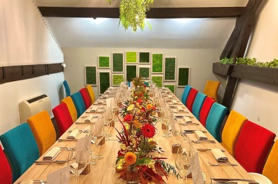 Miniature Location salle Voisins-le-Bretonneux (Yvelines) - La Ferme de Voisins #42 Table dressée avec des verres, couverts et serviettes, entourée de chaises colorées dans une salle lumineuse avec…