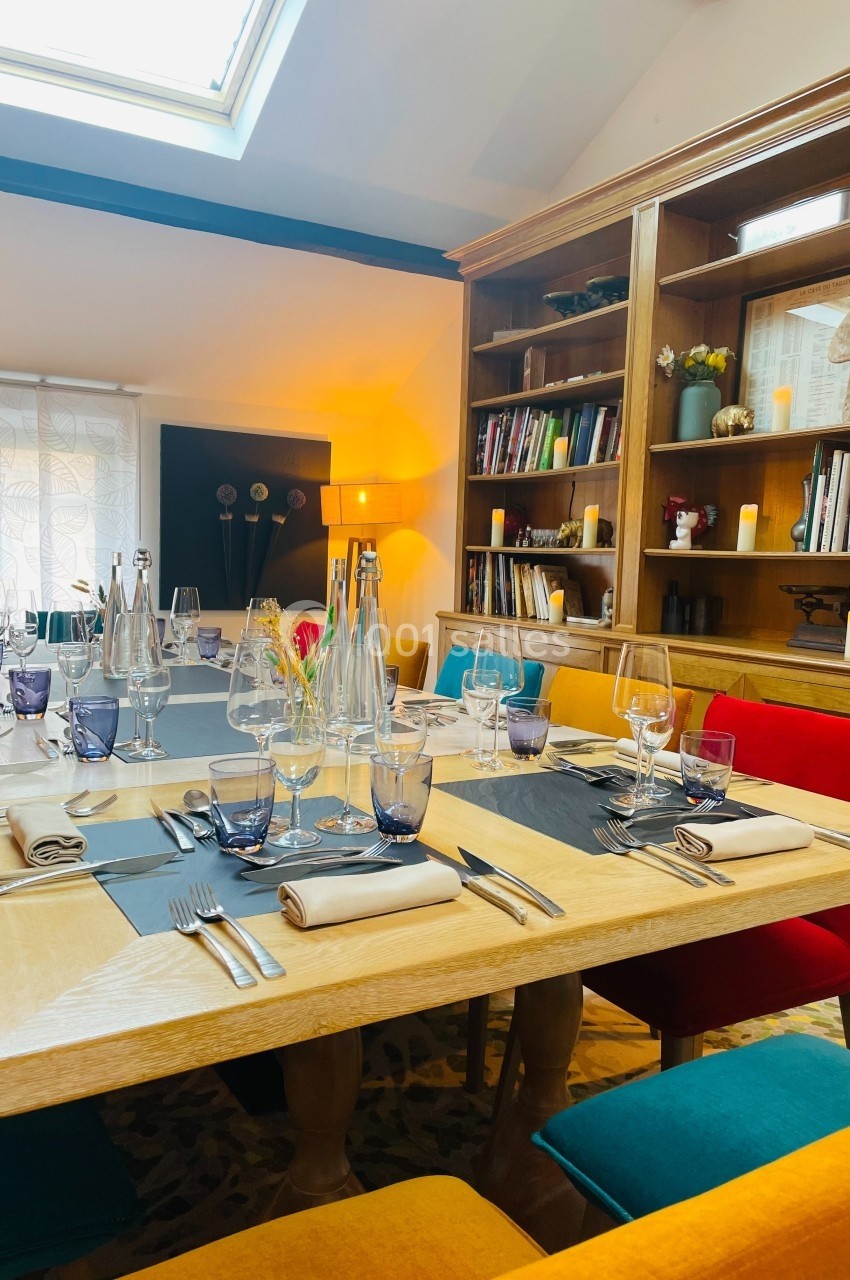Table dressée avec des verres, couverts et serviettes, entourée de chaises colorées dans une salle lumineuse avec…