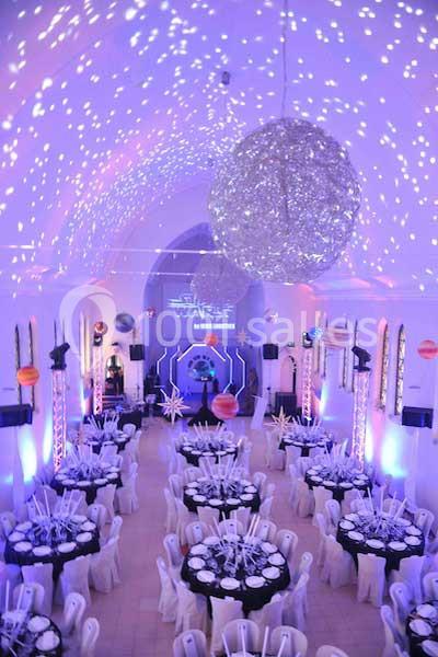 Salle décorée sur le thème spatial avec des tables dressées, des lumières colorées et des éléments suspendus évoquant l…