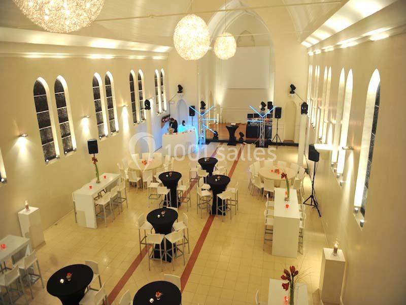 Salle de réception lumineuse avec tables rondes et rectangulaires, décor moderne et éclairage suspendu.