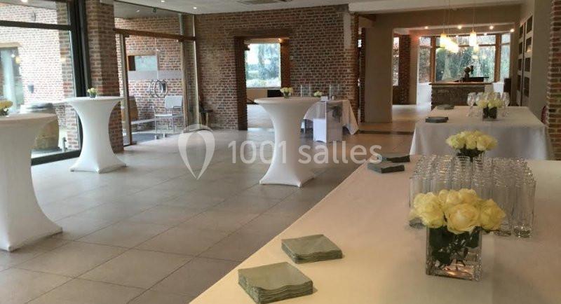 Location salle Brunehaut (Hainaut) - Le Clos de la Conciergerie #6 Salle lumineuse avec tables hautes couvertes de nappes blanches, décorée de bouquets de roses blanches.