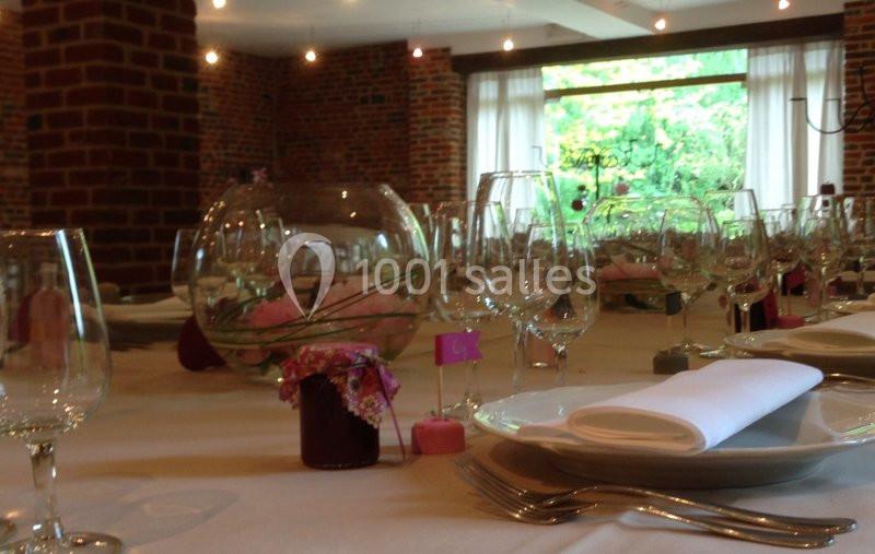 Location salle Brunehaut (Hainaut) - Le Clos de la Conciergerie #8 Tables dressées avec nappes blanches, verres, assiettes et décorations florales dans une salle en briques avec vue sur un…