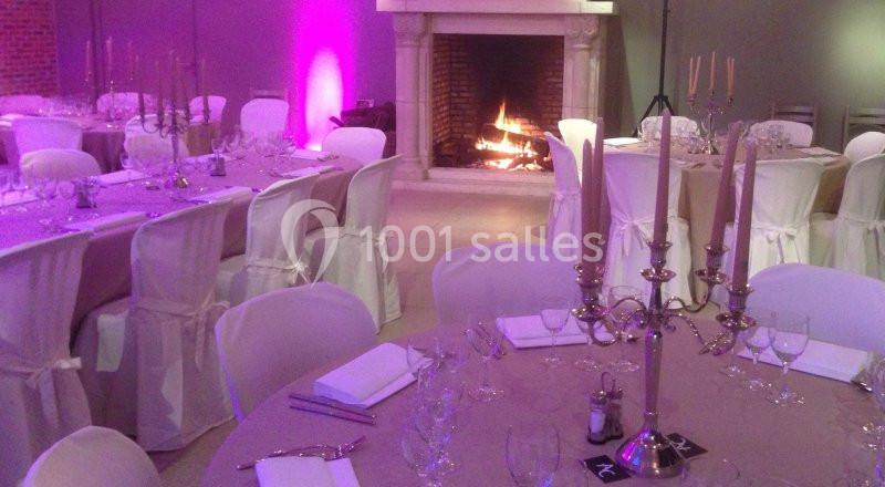 Location salle Brunehaut (Hainaut) - Le Clos de la Conciergerie #9 Salle de réception décorée avec des tables dressées, des chaises blanches et une cheminée allumée en arrière-plan.