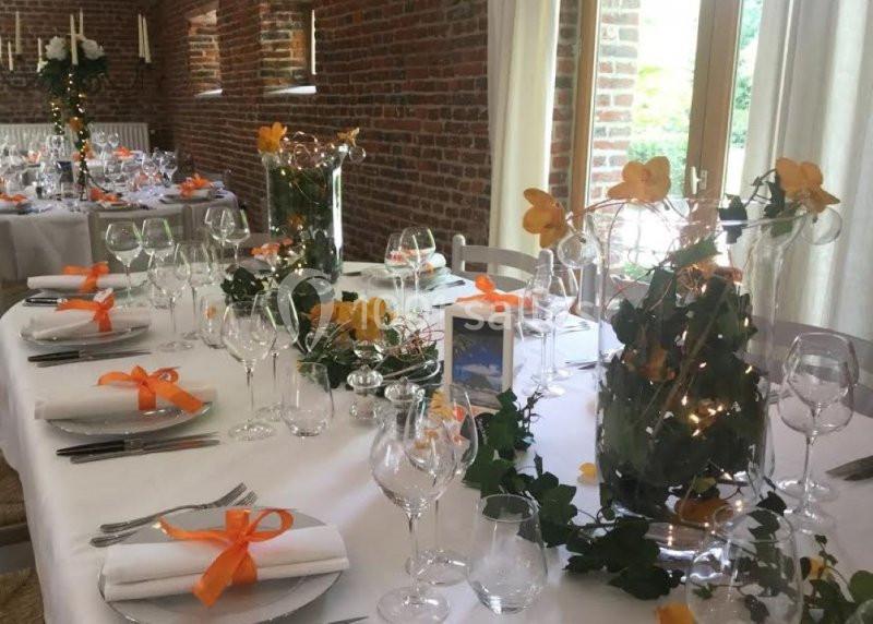 Location salle Brunehaut (Hainaut) - Le Clos de la Conciergerie #12 Table décorée pour un événement avec nappes blanches, fleurs orange, rubans assortis et verrerie élégante.