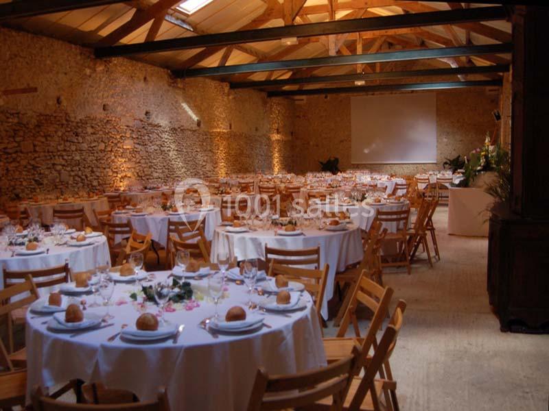 Salle de réception en pierre avec tables rondes dressées pour un repas, éclairage chaleureux et écran en fond.