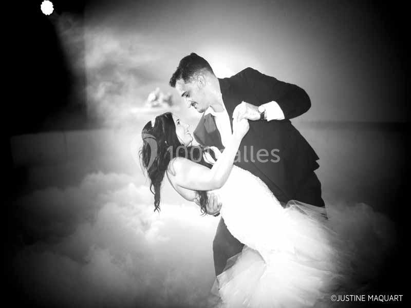 Un couple en tenue de mariage danse dans une ambiance romantique avec un fond de fumée et éclairage tamisé.