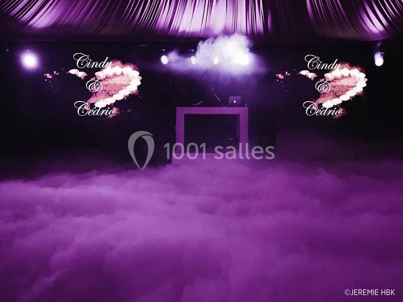Scène de mariage avec écran affichant ’Cindy & Cédric’, éclairage violet et sol recouvert de fumée.