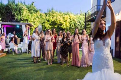 Une mariée lance son bouquet à un groupe de femmes rassemblées dans un jardin lors d'une réception en soirée.