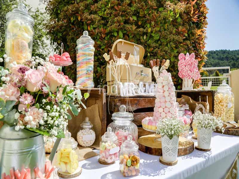 Table décorée avec des bonbonnières remplies de sucreries colorées, fleurs et éléments rustiques en extérieur.