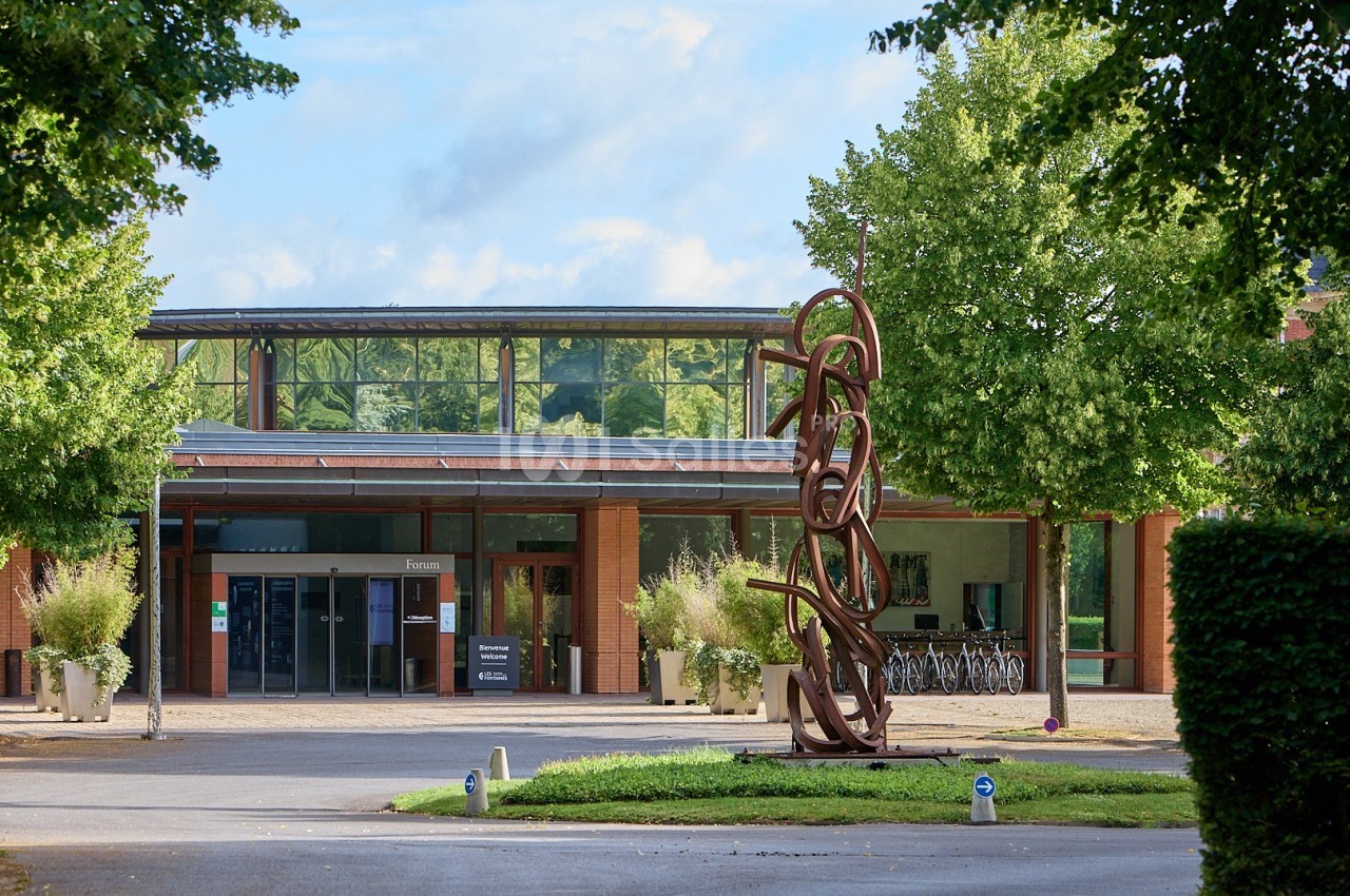 Entrée d'un bâtiment moderne avec une sculpture en métal devant et des arbres environnants.