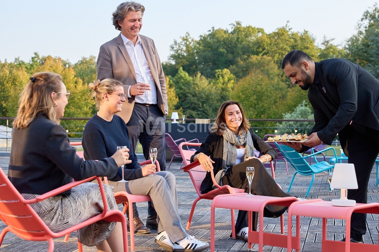 Un serveur propose des amuse-bouches à un groupe de personnes assises en extérieur sur une terrasse.