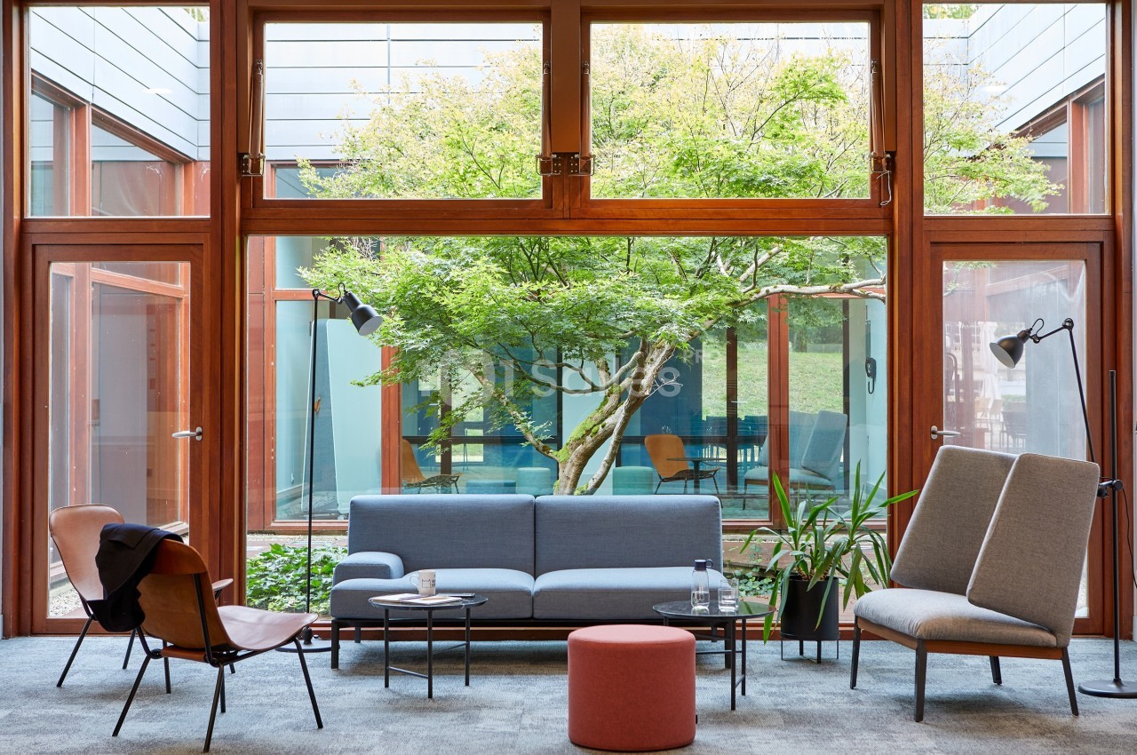 Salon moderne avec canapés, fauteuils et table basse, donnant sur un jardin arboré visible à travers de grandes baies…