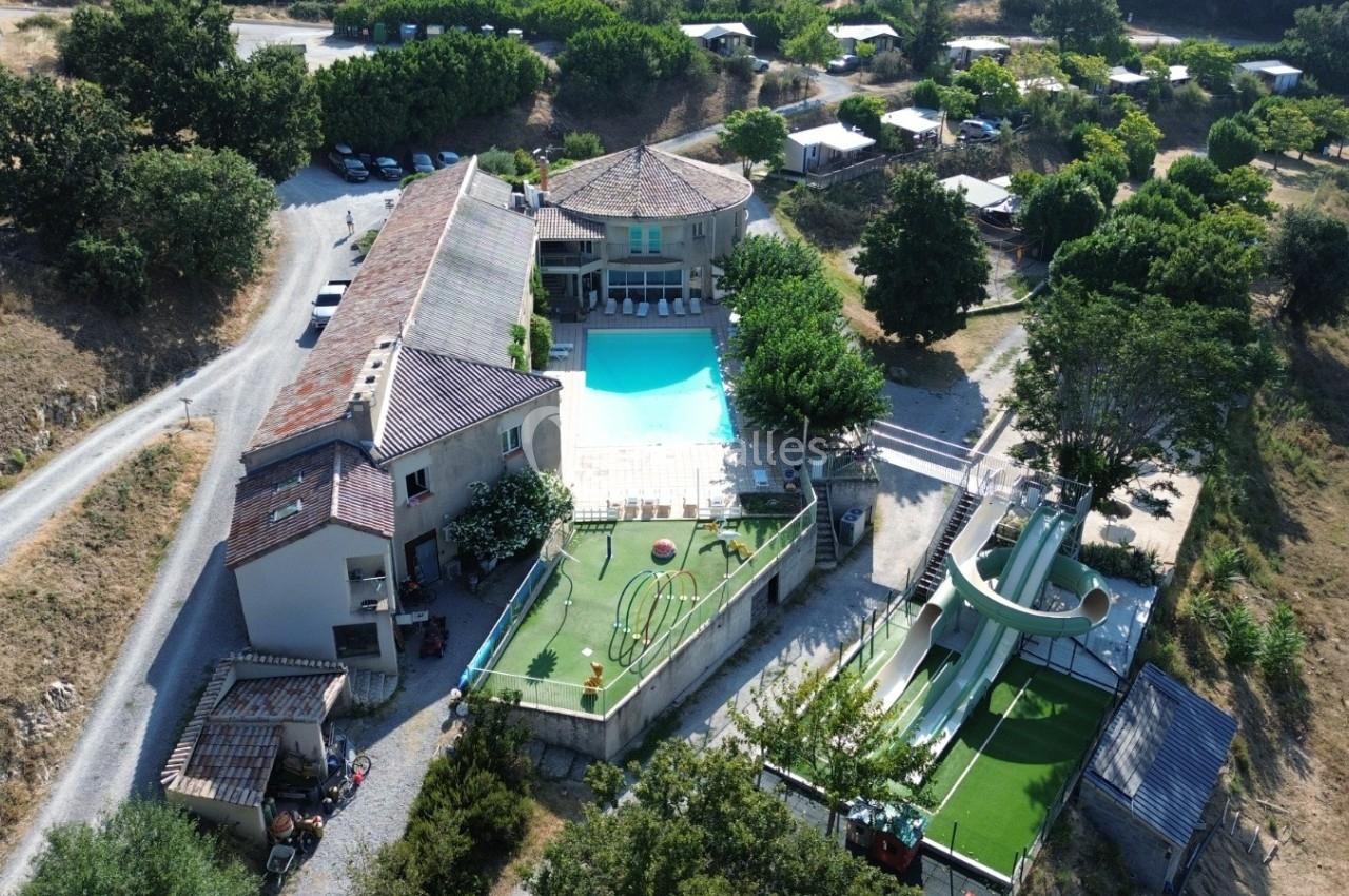 Vue aérienne d'un complexe avec piscine, toboggans aquatiques, bâtiments et espaces verts environnants.