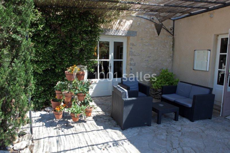 Salon de jardin avec fauteuils en rotin noir sur une terrasse en pierre, entouré de plantes et pots de fleurs.