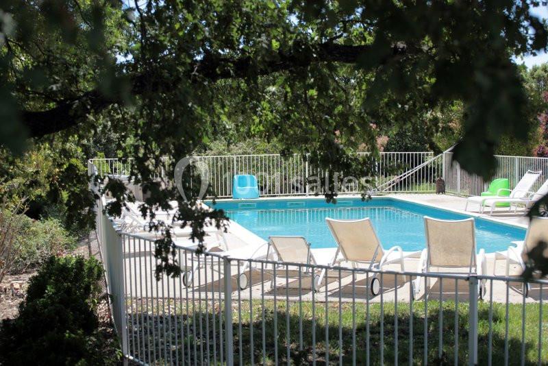 Piscine extérieure entourée de chaises longues et protégée par une barrière, partiellement ombragée par des arbres.